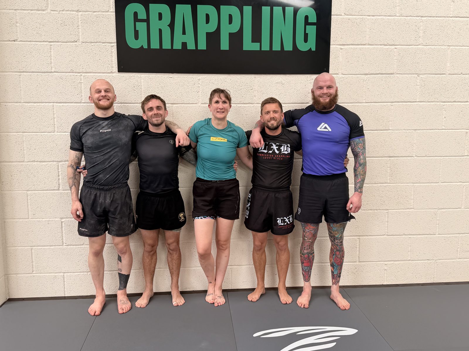 A group of members posing together under the Forged Grappling sign
